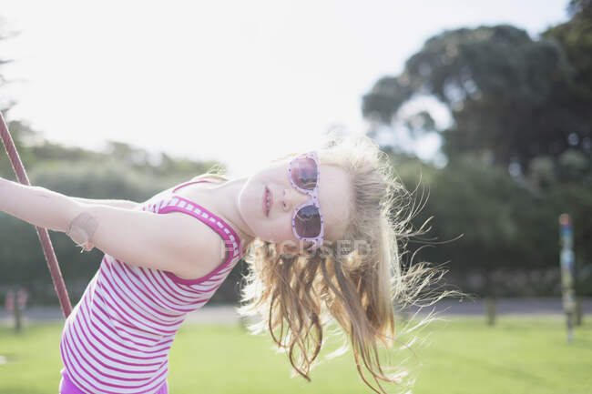 Young girl playing on swing wearing sunglasses — Stock Photo