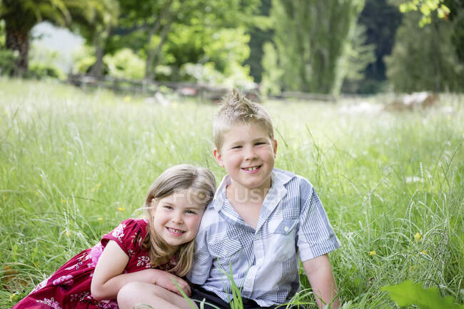 Joven niño y niña sentado en la hierba verde mirando a la cámara - foto de stock