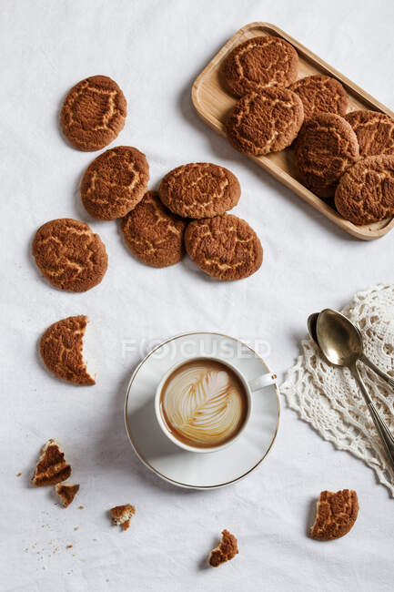 Vista superior de café caliente aromático con un dibujo hecho con crema y acompañado de muchas galletas caseras - foto de stock