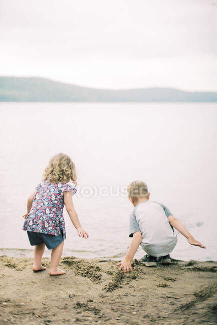 Dos niños jugando en la arena junto a la orilla de un lago - foto de stock
