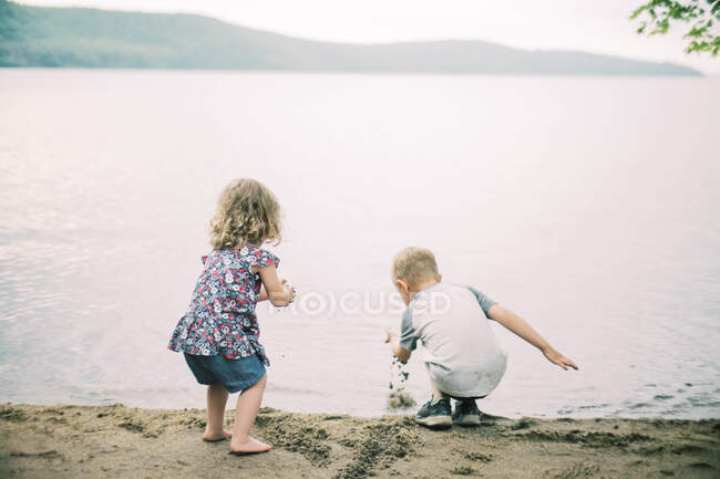 Двое детей играют на песке на берегу озера — стоковое фото