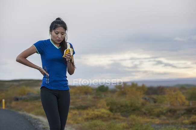 Hermosa mujer comiendo plátano durante el ejercicio en el área rural en Islandia - foto de stock
