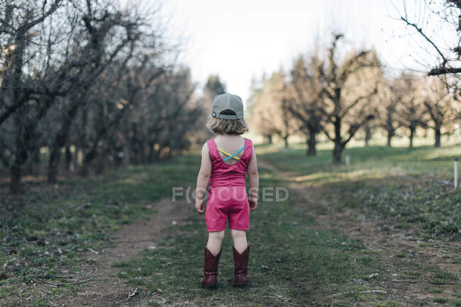 A young girl stands in an orchard wearing a leotard and cowgirl boots. — Stock Photo