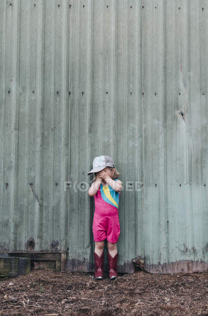 Una joven se para cerca de un granero con botas de cuero y vaquera. - foto de stock
