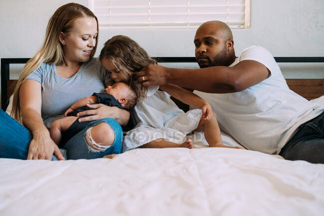 Многонациональная семья обнимается на кровати с новорожденным ребенком — стоковое фото