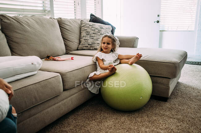 Молодая девушка сидит на большом шаре в гостиной и смотрит на кого-то — стоковое фото