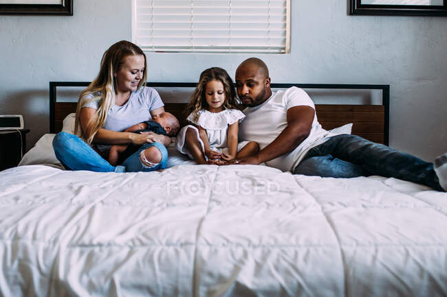 Una familia acurrucada en la cama con un bebé recién nacido - foto de stock