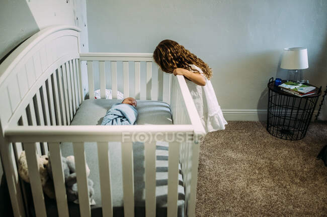 Junges Mädchen blickt über die Krippe auf neugeborenes Geschwisterchen — Stockfoto