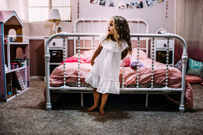 Young girl standing at the end of her bed looking away — Stock Photo