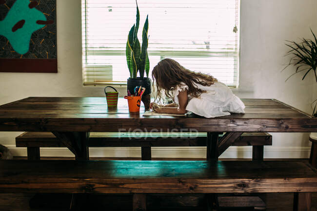 Young girl sitting on top of table coloring — Stock Photo