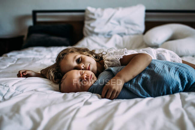 Portrait of young girl snuggling newborn brother — Stock Photo