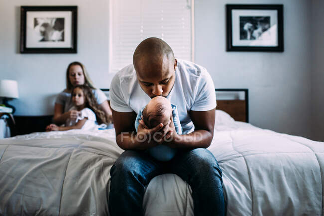 Center portrait of dad kissing newborn baby on bed — Stock Photo