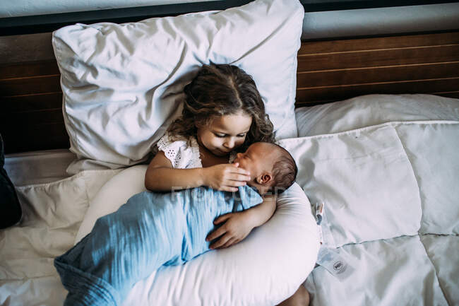 Joven chica sosteniendo recién nacido bebé hermano en la cama - foto de stock