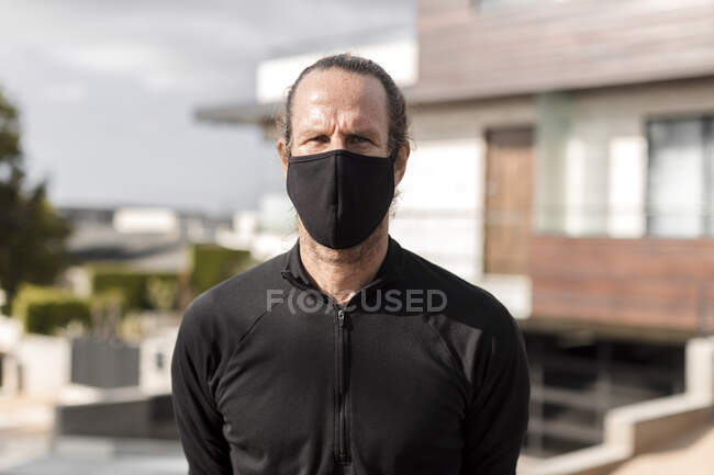 Retrato de um homem usando uma máscara de tecido em pé em um bairro — Fotografia de Stock