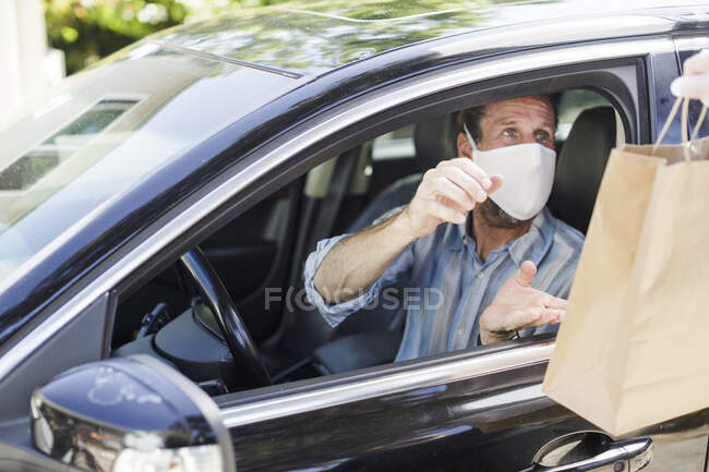 Borsa passata attraverso il finestrino dell'auto al conducente indossando maschera — Foto stock