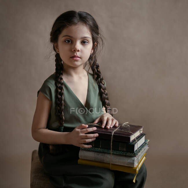 A girl with long pigtails sits and holds a stack of books in her lap — Stock Photo