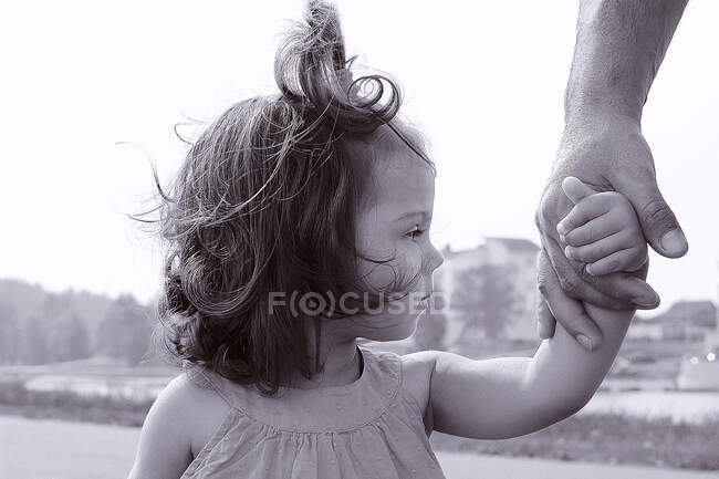 Uma menina segura a mão de seu pai contra o pano de fundo da cidade — Fotografia de Stock