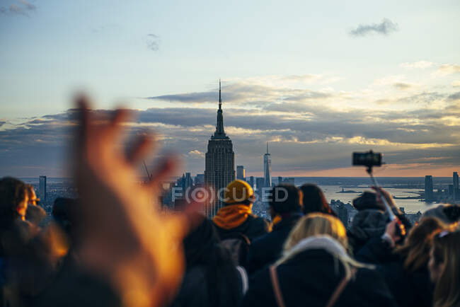 Люди смотрят с небоскребов на здания Нью-Йорка на закате и фотографируются с мобильным телефоном, США — стоковое фото