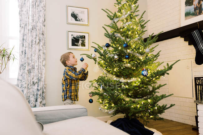 Niño pequeño poniendo adornos en su árbol de Navidad - foto de stock