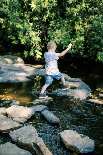Ein mutiger 5-Jähriger springt über Felsen in einem Fluss — Stockfoto