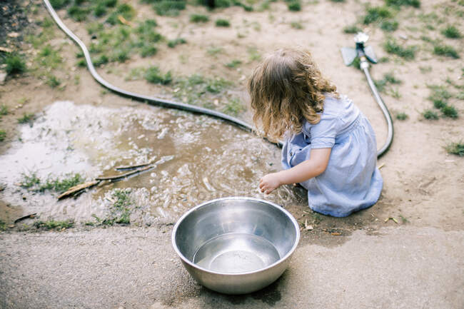 A toddler girl playing in a muddy puddle in her backyard — Stock Photo
