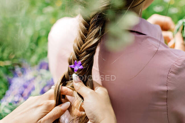 Fille tresse une fleur dans une tresse sur la nature — Photo de stock