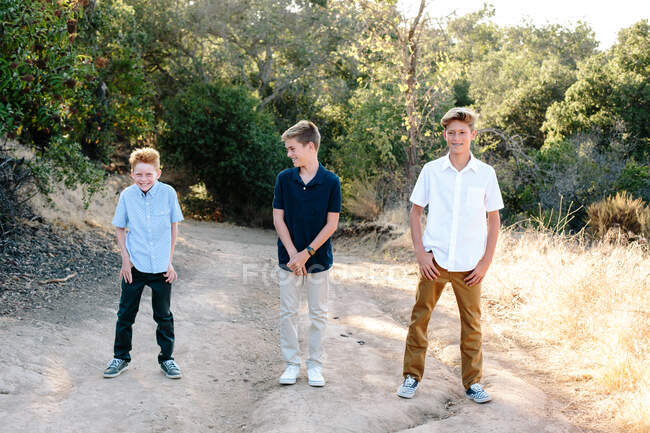 Três jovens irmãos ficam juntos fora de um trilho sorrindo — Fotografia de Stock