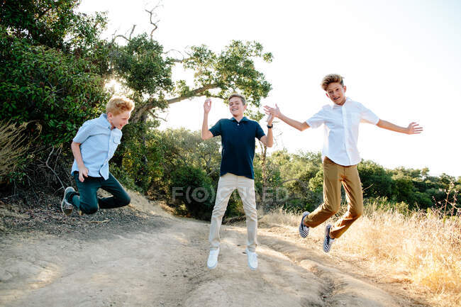 Tre ragazzi saltare in aria sorridendo mentre su un sentiero escursionistico — Foto stock