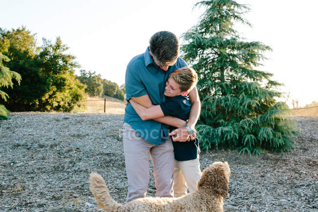 Un père et un fils adolescent embrassent alors qu'ils sont dehors avec leur chien hamster — Photo de stock