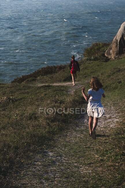 Девушка бежит в открытом пространстве по тропе к океану со своей матерью — стоковое фото