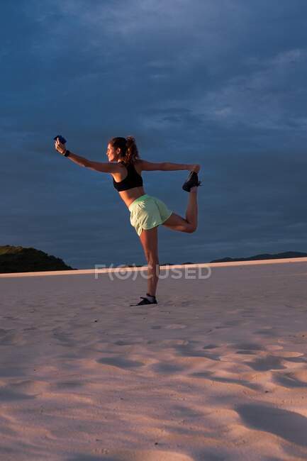 Woman making yoga pose at sunset in sand dunes — Stock Photo