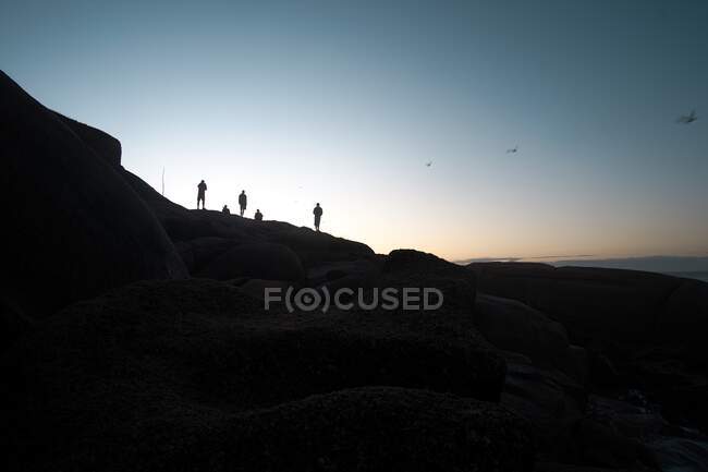Silhouette di persone che guardano il sole sorgere sulla costa — Foto stock