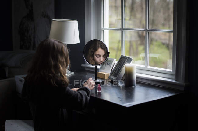 Jeune fille peignant ses ongles dans la lumière de la fenêtre — Photo de stock