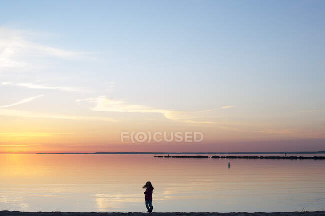 Silueta de niña en la playa al amanecer - foto de stock