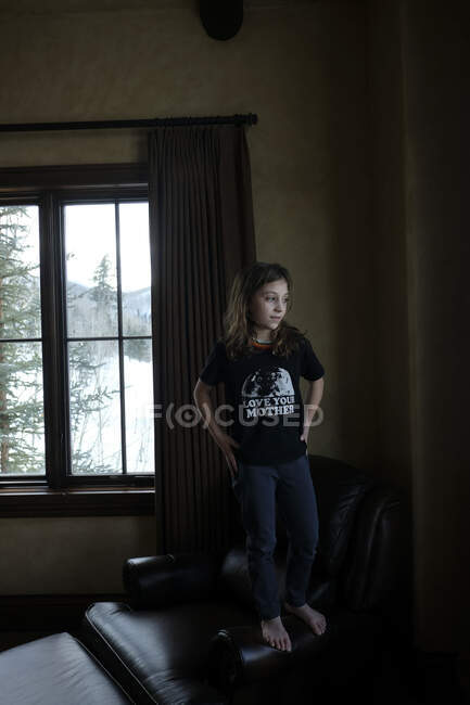 Девушка, стоящая на стуле и выглядывающая в окно — стоковое фото