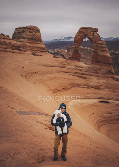 A man with a child is standing near Delicate arch at Arches NP — Stock Photo