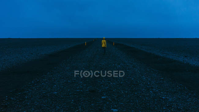 Wanderer in leuchtend gelbem Mantel ging den vulkanschwarzen Sandweg hinunter — Stockfoto