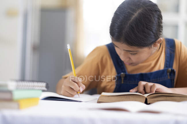 Asiatico ragazza lettura e fare i compiti a casa sua — Foto stock