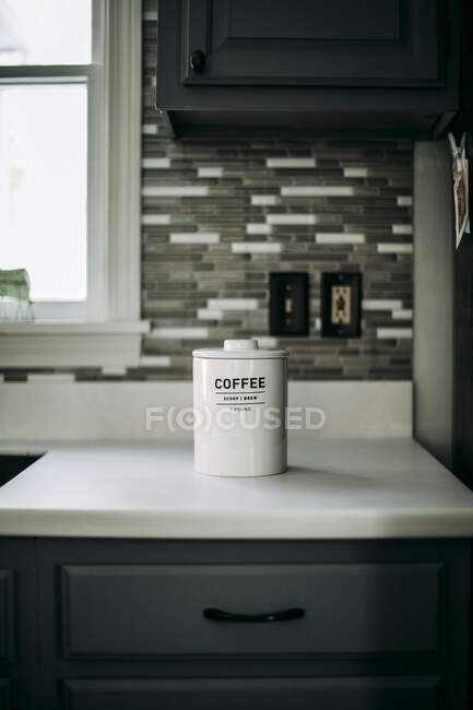Ein weißes Glas gemahlenen Kaffees sitzt auf einer weißen Arbeitsplatte in einer Küche. — Stockfoto