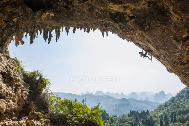Hombre escalando el arco en la guarida de Odín junto a la colina de la Luna en Yangshuo - foto de stock