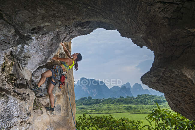Joven escaladora escalando en zona remota en Yangshuo, China - foto de stock