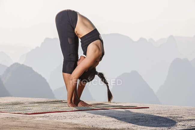 Joven hermosa mujer practicando yoga con vista a la montaña en el fondo. - foto de stock