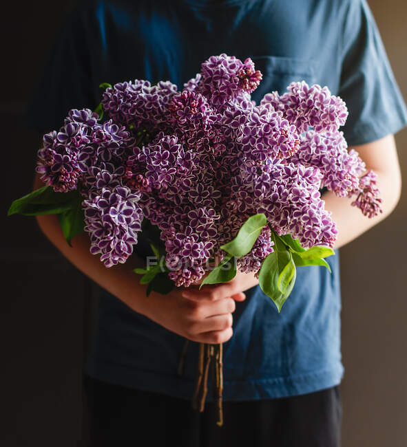 Young boy holding a bouquet of purple lilac flowers — Stock Photo