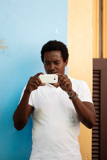 Чорний чоловік фотографує зі своїм мобільним телефоном, кубик — стокове фото