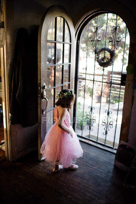 Молода дівчина стоїть біля вхідних дверей у навчальному посібнику та квітковій короні — стокове фото