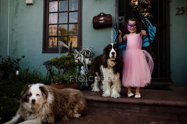 Young girl in dress up standing on porch with dogs — Stock Photo