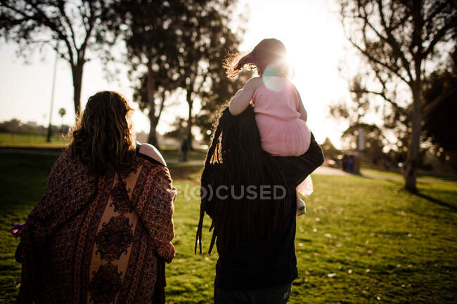Niece on uncle's shoulders walking with aunt and sunset — Stock Photo