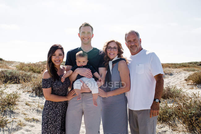 Familia de cinco sonriendo en la playa con sol detrás - foto de stock