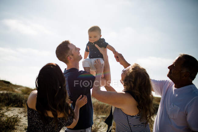 Papa hält Baby hoch, während Familie am Strand lächelt — Stockfoto