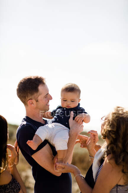 Pai segura bebê como família sorri na praia — Fotografia de Stock